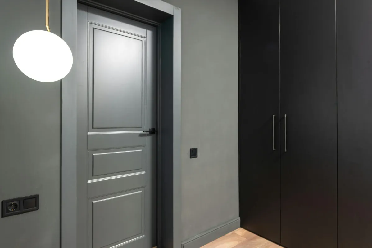 Modern gray interior hallway with a paneled door and black cabinets